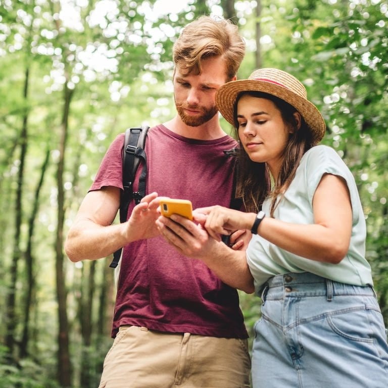 Kostenlose Wander-App: Junger Mann und junge Frau schauen im Wald auf ein Smartphone (Foto: picture-alliance / Reportdienste, picture alliance / Zoonar | Elizaveta Tomashevska)